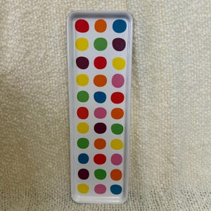 May include: A rectangular white metal tray featuring a repeating pattern of colorful polka dots in shades of red, orange, yellow, green, blue, purple, and pink arranged in three vertical columns across the surface of the tray.