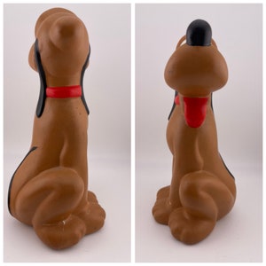 Puede incluir: Una figurita de perro de cer&aacute;mica marr&oacute;n con orejas negras y un collar rojo. El perro est&aacute; sentado con la cabeza inclinada hacia arriba, mirando hacia un lado.