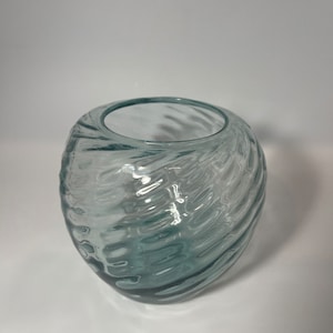 May include: A clear glass vase with a swirling, textured design. The vase is oval shaped and has a wide opening.