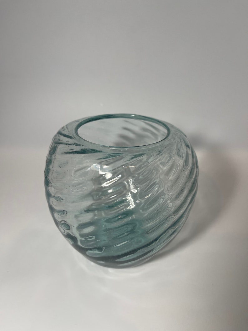 May include: A clear glass vase with a swirling, textured design. The vase is oval shaped and has a wide opening.