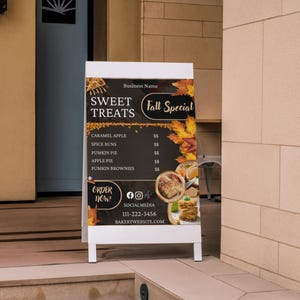 May include: A-frame sign advertising "Sweet Treats" and "Fall Special." The sign features a dark background with autumn leaves and images of baked goods. Menu items include caramel apple, spice buns, pumpkin pie, apple pie, and pumpkin brownies.