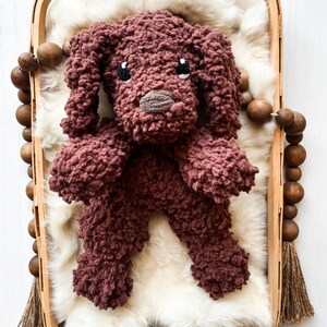 May include: A plush brown dog toy with black eyes and a brown nose, lying on a white faux fur bed inside a wooden basket.