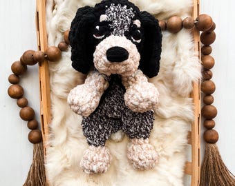 May include: A handmade crochet plush dog toy featuring a black and white speckled body, solid black ears, and a tan muzzle. The stuffed animal has a black nose and dark eyes, crafted from soft yarn with a textured, fuzzy appearance.