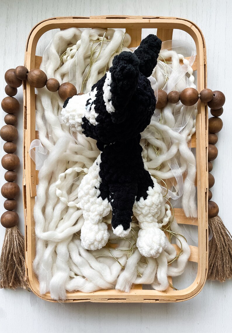 May include: A black and white crocheted dog toy in a wooden basket with white yarn and brown wooden beads.