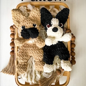 May include: Two crocheted stuffed dog toys in a wooden basket. One dog is tan and the other is black and white.
