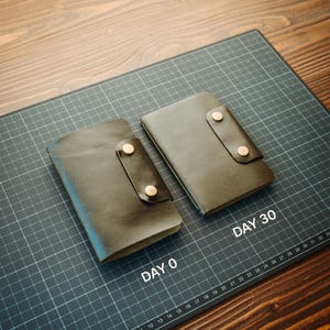 May include: Two dark brown leather notebook covers with snap closures. One is labelled DAY 0 and the other is labelled DAY 30, resting on a black cutting mat with a white grid. The covers feature a smooth texture and two metallic snap buttons each.