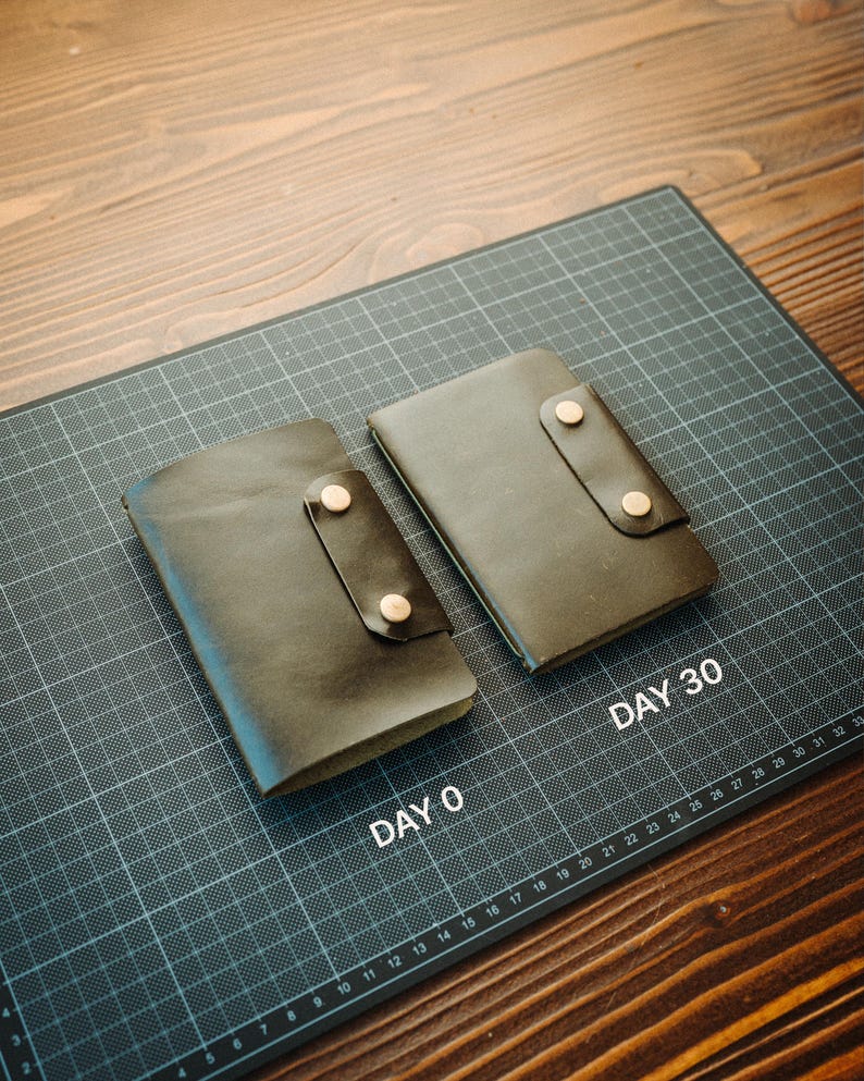 May include: Two dark brown leather notebook covers with snap closures. One is labelled DAY 0 and the other is labelled DAY 30, resting on a black cutting mat with a white grid. The covers feature a smooth texture and two metallic snap buttons each.