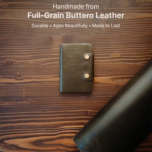May include: A dark brown leather wallet featuring a vertical strap secured by two metallic snap buttons. The text above reads: Handmade from Full-Grain Buttero Leather. Durable &bull; Ages Beautifully &bull; Made to Last. The wallet is rectangular.