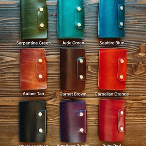 May include: Nine rectangular leather wallets with snap closures, arranged in a grid. Colours include Serpentine Green, Jade Green, Saphire Blue, Amber Tan, Garnet Brown, Carnelian Orange, Obsidian Black, Amethyst Purple, and Ruby Red.