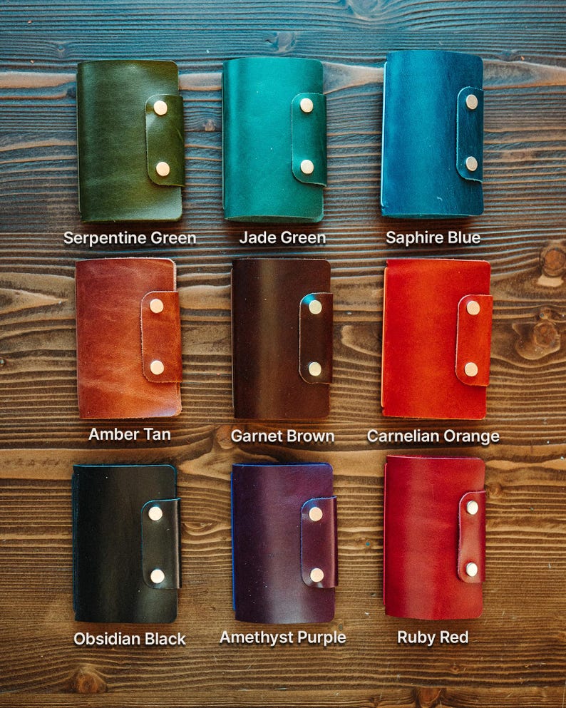 May include: Nine rectangular leather wallets with snap closures, arranged in a grid. Colours include Serpentine Green, Jade Green, Saphire Blue, Amber Tan, Garnet Brown, Carnelian Orange, Obsidian Black, Amethyst Purple, and Ruby Red.