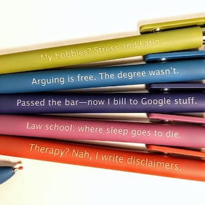 Puede incluir: Un conjunto de bolígrafos coloridos con frases humorísticas impresas. Los bolígrafos son de color verde, azul, morado, rosa y naranja. El texto incluye frases como "My hobbies? Stress and Latin" y "Therapy? Nah, I write disclaimers."
