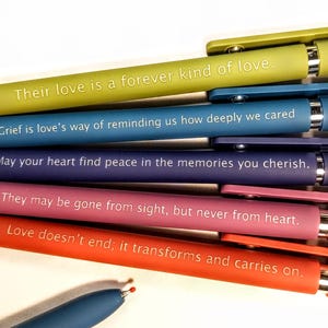 May include: A collection of colorful pens in shades of green, blue, purple, pink, and orange. Each pen has a different inspirational quote printed in white. The pens are a writing instrument.