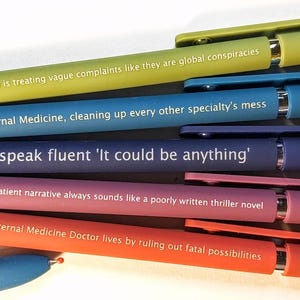 Peut inclure: Un ensemble de cinq stylos à bille rétractables de couleur vert lime, bleu, violet foncé, mauve et orange, chacun portant un texte imprimé en blanc sur la médecine interne. Un stylo bleu partiel est visible en bas à gauche de l'ensemble.