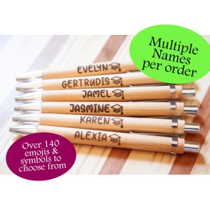 May include: A set of eight bamboo pens with silver accents. Each pen is engraved with a different name and a graduation cap symbol. The text "Multiple Names per order" is visible in the top right corner of the image. The text "Over 140 emojis & symbols to choose from" is visible in the bottom left corner of the image.