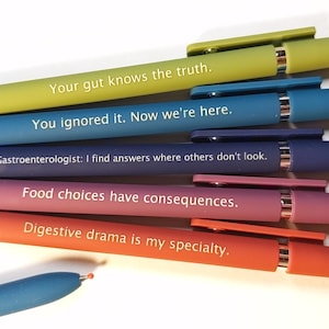 Könnte beinhalten: Eine Sammlung farbenfroher Stifte mit humorvollen Aufschriften. Die Stifte sind in Gelb-, Blau-, Lila-, Rosa- und Orangetönen gehalten. Der Text enthält Sätze wie "Your gut knows the truth" und "Digestive drama is my specialty."