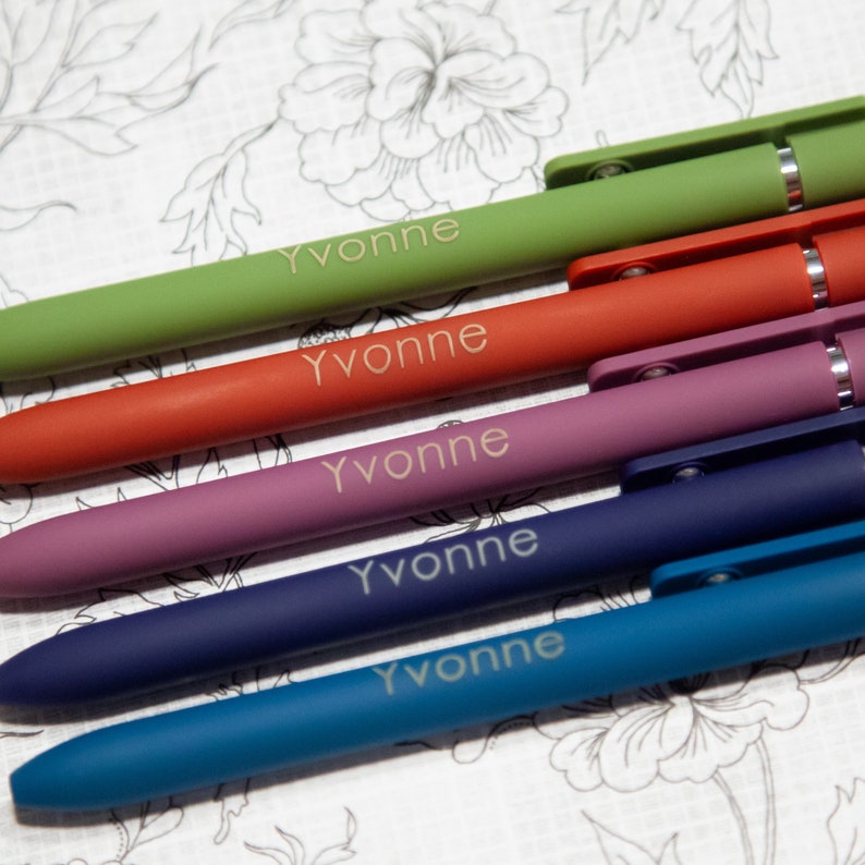 Five different colored pens with text on them on a floral background