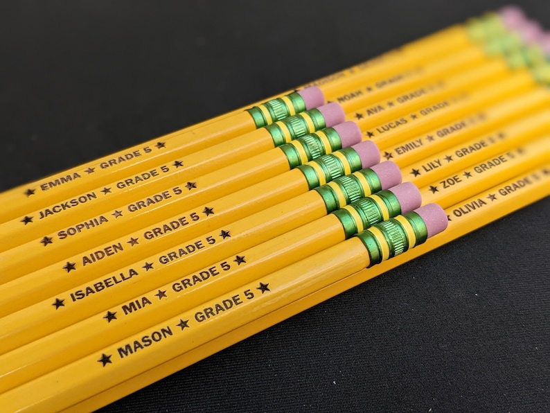 May include: A selection of yellow pencils, each with a pink eraser and green and gold ferrule. The pencils are printed with names and "GRADE 5". The pencils are arranged in a row. Ideal for school supplies, each pencil is approximately 19 cm long.