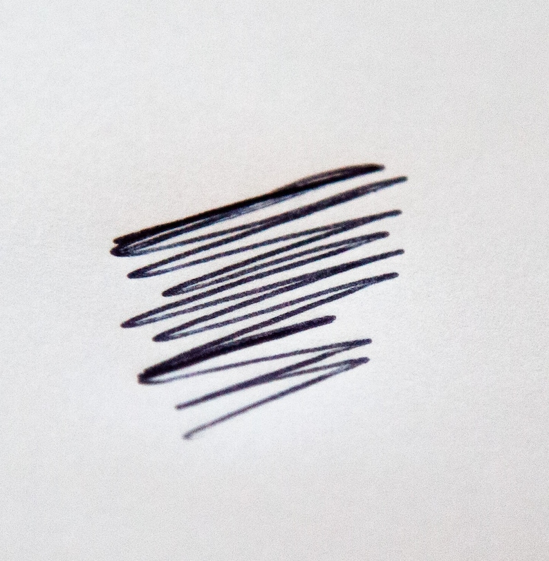 May include: A close-up of a white surface with a cluster of dark blue, scribbled lines. The lines are roughly parallel and angled, creating a textured, abstract design. The lines are thick and appear to be made with a marker.