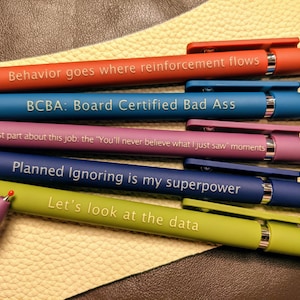 May include: Six colorful pens with different motivational quotes printed on them. The quotes are: "Behavior goes where reinforcement flows", "BCBA: Board Certified Bad Ass", "Best part about this job, the "You'll never believe what I just saw" moments", "Planned Ignoring is my superpower", and "Let's look at the data".