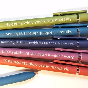 May include: A set of six retractable ballpoint pens in various matte colors including lime green, blue, dark blue, purple, and orange. Each pen features white printed text with medical-themed phrases such as I diagnose while you're still guessing, I see right through people... literally, Radiologist: Finds problems no one else can see, If it's subtle, I'll still catch it—don't worry, and Your secrets glow under my watch.
