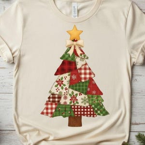 Op de afbeelding: Crèmekleurig T-shirt met een patchwork kerstboomontwerp. De boom bestaat uit rood, groen en wit gekleurde driehoeken, bekroond met een gouden ster en een crèmekleurige strik. De boomstam is bruin.