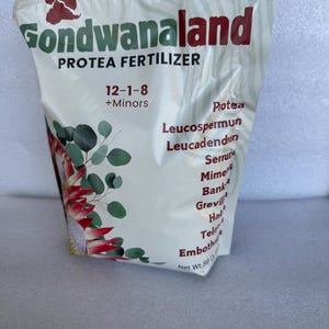 May include: A white bag of Gondwanaland Protea Fertilizer with a 12-1-8 NPK ratio and a list of plants it is suitable for, including Leucospermum, Leucadendron, Serruria, Mimetes, Banksia, Grevillea, Hakea, Telopea, and Embothrium. The bag has a picture of a red and green Protea flower.