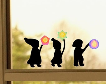 Peut inclure: Trois silhouettes noires de personnages tenant des lanternes en papier colorées. Les lanternes sont en forme d'étoiles et de cercles et présentent un dégradé arc-en-ciel.
