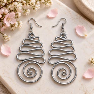 May include: A pair of silver-toned metal dangle earrings featuring a continuous wire design that forms a series of stacked horizontal loops, culminating in a circular spiral at the base, suspended from simple curved ear wires for pierced ears.