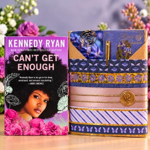 May include: A book titled Can't Get Enough by Kennedy Ryan featuring a portrait of a person with an afro surrounded by pink flowers, next to a decorative purple stationery set with a gold rose wax seal and a gold pen.