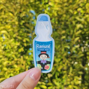Peut inclure: Un autocollant bleu et blanc repr&eacute;sentant une bouteille de Ramune avec un personnage de dessin anim&eacute; sur l'&eacute;tiquette. L'&eacute;tiquette indique "Ramune Turnip Head" et "Made with Real Sugar".