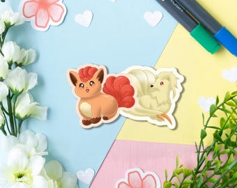Könnte beinhalten: Ein gestanzter Vinyl-Aufkleber mit zwei fuchsartigen Cartoon-Kreaturen. Links eine kleine orangefarbene Kreatur mit einem lockigen roten Schwanz. Rechts eine größere, cremefarbene Kreatur mit mehreren fließenden Schwänzen und roten Augen im weichen Stil.