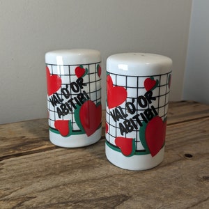 May include: Two white ceramic salt and pepper shakers with a black and white grid pattern and red hearts. The shakers have the text "Val'o'r Abitibi" on them.