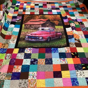 May include: A colourful patchwork quilt with a central panel featuring a red vintage pickup truck parked in front of a rustic barn. The truck has the words "Powell's Grocery" on the side and the number plate "AT 694".