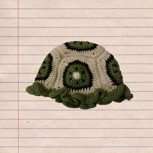 May include: A handmade crochet hat with a kiwi fruit design. The hat features a beige base with green and black accents, and a ruffled brim. The hat is a unique accessory.