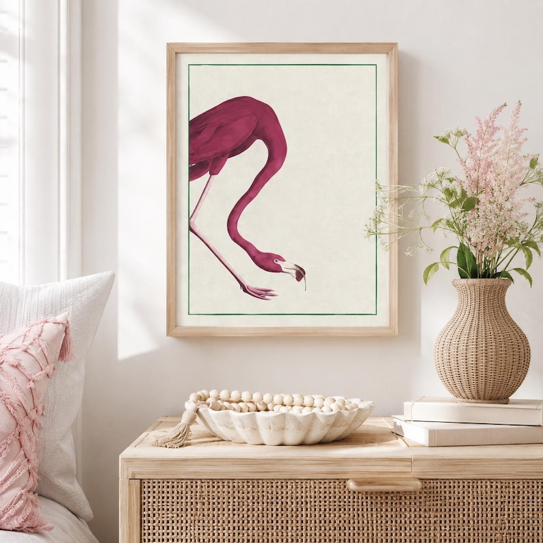 May include: A framed wall art print featuring a deep magenta flamingo with a curved neck, depicted in a minimalist style against a cream background. The illustration is enclosed within a thin green rectangular border, creating a clean visual focus.