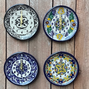 May include: Four Talavera ceramic wall clocks with blue and white designs. Each clock has a different floral pattern and features gold-colored hands.