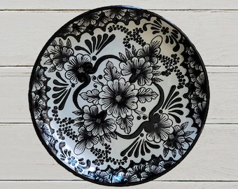 May include: A white ceramic plate with a black floral design. The plate features intricate details and a traditional Mexican style.
