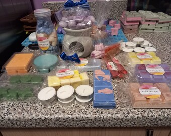 May include: Assortment of wax melts in various colors and scents, including lavender, orange, and green. The wax melts are packaged in clear plastic bags with labels. There are also tealight candles and a wax warmer.