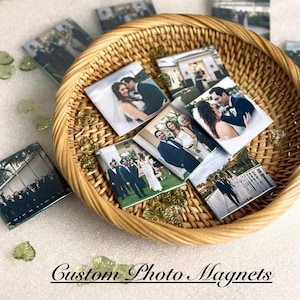May include: A wicker basket filled with square photo magnets featuring wedding photos. The magnets are arranged in a circular pattern and feature a variety of poses, including a couple kissing, a group photo of the wedding party, and a photo of the bride and groom walking down the aisle. The text "Custom Photo Magnets" is printed below the basket.