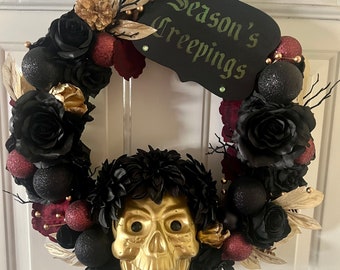 May include: A black and gold Halloween wreath with black roses, gold leaves, and red berries. A gold skull with black eyes is in the center of the wreath. A black sign with white text reads "Season's Creepings".