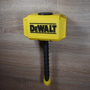 Op de afbeelding: Een gele en zwarte hamer met het woord "DEWALT" in zwarte letters. De hamer heeft een zwarte steel en een gele kop. De hamer is een gereedschap.