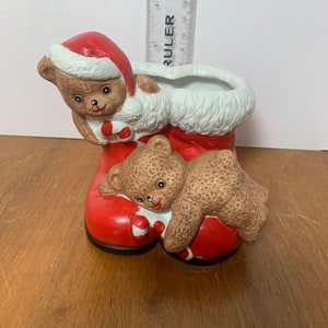 May include: A ceramic Christmas boot planter with two teddy bears wearing Santa hats and holding candy canes. The boot is red with white fur trim.