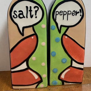 May include: A set of ceramic salt and pepper shakers shaped like lips with a speech bubble above each. The salt shaker says "salt?" and the pepper shaker says "pepper!" The shakers are decorated with green, orange, red, white, and blue.
