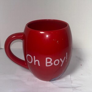 May include: A glossy red ceramic mug with a rounded shape and a curved handle. The mug features the white text "Oh Boy!" on its side. The mug is designed for hot beverages and is suitable for home or office use.