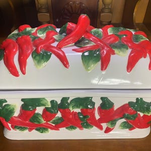 Puede incluir: Caja de pan de cerámica blanca con un diseño de chiles rojos y verdes. La tapa está decorada con chiles rojos y hojas verdes.