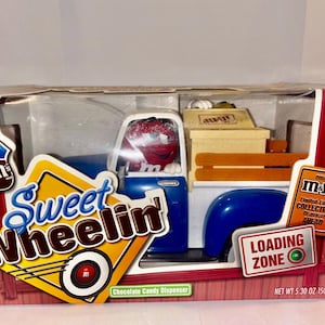 Puede incluir: Dispensador de caramelos de chocolate M&M's Sweet Wheelin' con diseño de camión coleccionable. El camión es azul y blanco con un personaje M&M's rojo en el asiento del conductor. El embalaje incluye el texto "Loading Zone" y "Limited Edition".