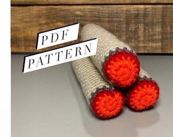 May include: A crochet pattern for a campfire with three logs. The logs are crocheted in a beige yarn with red and gray accents. The text "PDF PATTERN" is visible in the image.