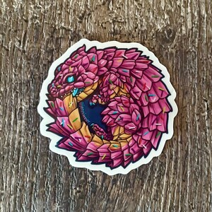 May include: A pink and yellow cartoon pangolin curled up in a ball, covered in colourful sprinkles. The pangolin has a blue eye and a white background. The text "@jenniweee" is visible on the image.