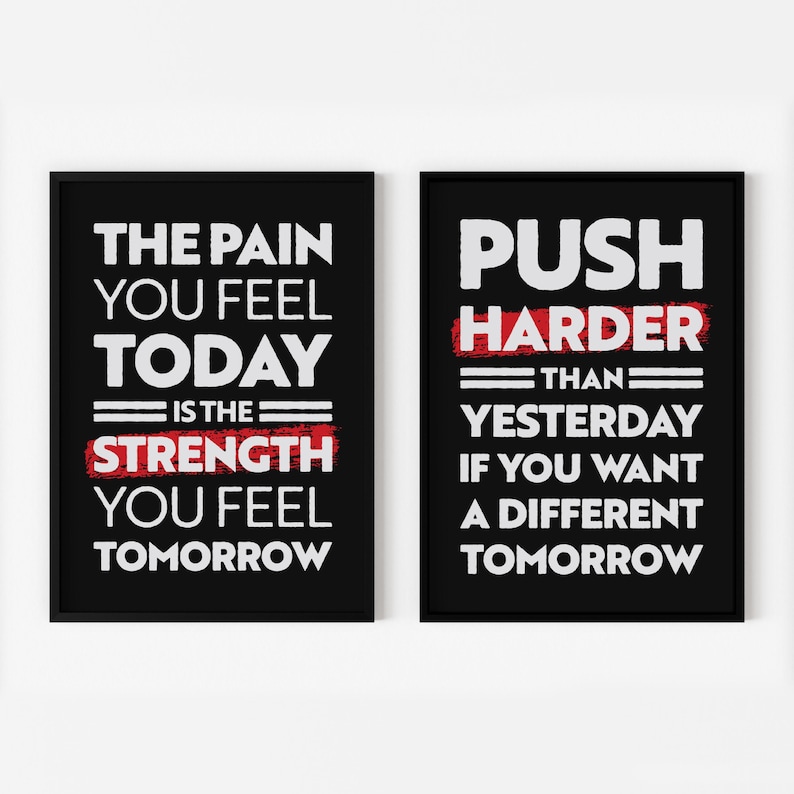 May include: Two black framed motivational posters with white text on a white background. The left poster says "The pain you feel today is the strength you feel tomorrow". The right poster says "Push harder than yesterday if you want a different tomorrow".