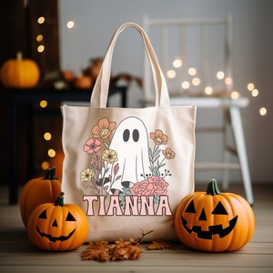 May include: A beige tote bag with a ghost and floral design. The bag has the name "Tianna" printed on it in pink letters.